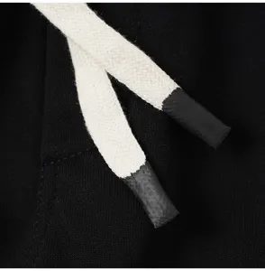 Minimalist black apparel detail shot featuring long beige drawstrings with dipped ends.