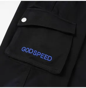 Black cargo shorts pocket detail with blue Godspeed embroidery and metal snap button.