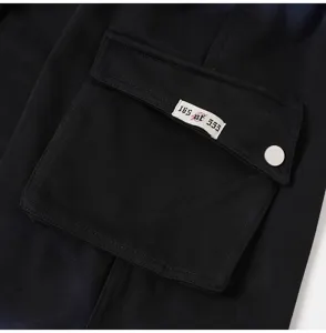 Detailed shot of black cargo shorts pocket with custom numbered woven label and metal snap.