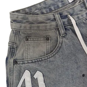 Close-up of distressed denim shorts with drawstring and applique number eleven detail.