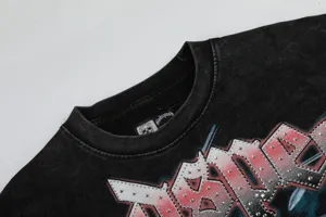 Gros plan sur le t-shirt noir vintage lavé avec étiquette de col et motif strass sur la poitrine.