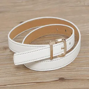 White thin leather belt detail close up, showing fine texture and golden metal pin buckle design.