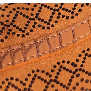 Dettaglio di una cintura larga da donna in ecopelle perforata marrone con texture coccodrillo in rilievo.