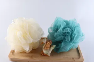 Detailed view of soft PE mesh bath sponge loofah in beige and teal colors on wooden tray.