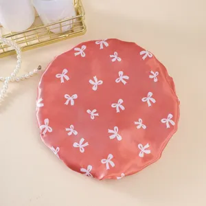 Close-up detail of coral satin waterproof shower cap featuring cute white bow print.