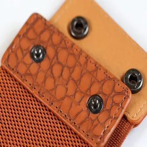 Dettaglio cintura elastica marrone con pelle effetto coccodrillo e bottoni a pressione.