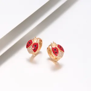 Primo piano di orecchini a cerchio coccinella in smalto rosso dorato con zirconi lucenti.