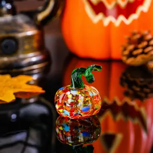 Detailed shot of a colorful glass pumpkin figurine with green stem on a reflective tabletop.