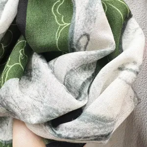 Vue rapprochée montrant la texture douce et le motif de camélia vert de cet élégant foulard.