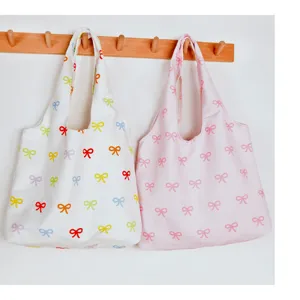 Detailed view of cute bow print canvas tote bags hanging on wall hook, casual style.