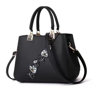 Vista detallada del bolso de cuero negro con delicado bordado floral y herrajes metálicos finos.