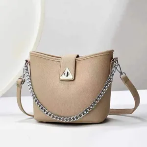Détail de sac seau beige minimaliste montrant la bandoulière en chaîne et le verrou triangulaire.