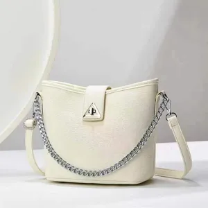 Sac seau minimaliste avec bandouliere en chaine et fermoir triangulaire elegant.