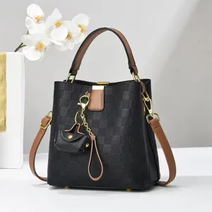 Close-up detail of stylish black checkered bucket bag with brown accents and mini pouch charm.