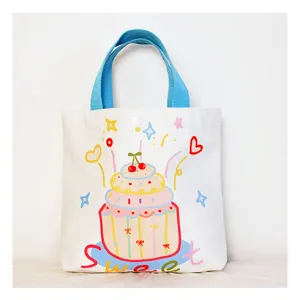 Closeup of the cute white canvas handbag featuring blue handles and sweet cake graphic detail.