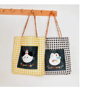 Vista dettagliata della borsa tote a quadri con graziosi patch in denim di gatto e coniglio.
