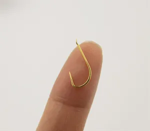 Mini barbless golden fishing hook close up on finger, thin wire xue hook for carp fishing.