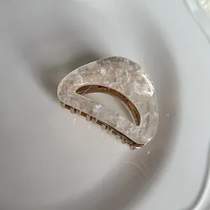 Detailweergave van een parelwitte acetaat haarklem met holle boog en gouden tanden.
