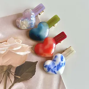 Closeup view of acetate heart hair clips, featuring marbled pattern and durable duckbill design.