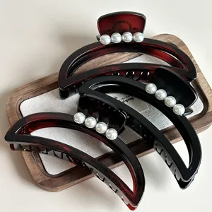 Close-up detail of stylish crescent hair claw clips with pearls, elegant tortoise and black design.