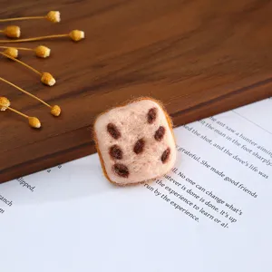 Close-up detail of handmade wool felt square cookie charm with brown spots on book page.