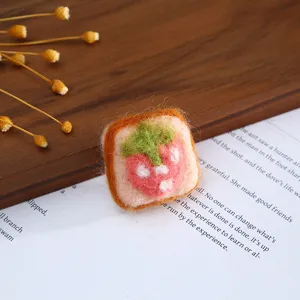 Close-up detail of handmade wool felt strawberry toast accessory on wooden background with paper.