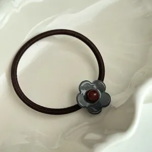Vue rapprochée du joli petit élastique à cheveux fleur avec pétale gris et perle rouge.