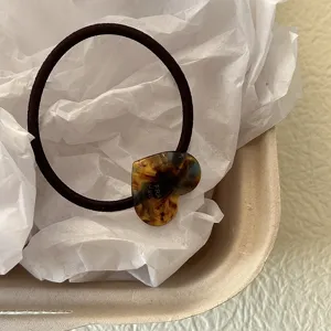 Primo piano di un elastico per capelli marrone con ciondolo a cuore in acetato tartarugato, dettaglio.