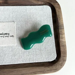Dettaglio molletta per capelli in acetato verde ondulato con superficie lucida e design unico.