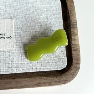 Dettaglio ravvicinato di molletta per capelli in acetato verde ondulato lucido e particolare.