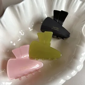 Close-up detail of three colorful acetate hair claws neatly placed in a white shell tray.