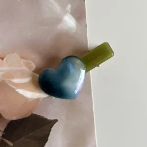 Detailed close-up of a blue gradient acetate heart hair clip with green duckbill handle design.