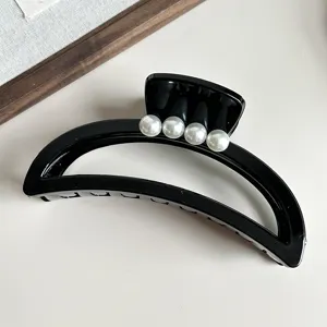 Detailed shot of black crescent hair claw clip featuring white pearls, minimalist aesthetic