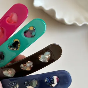 Close-up detail shot of colorful acetate hair clips featuring cute hollow heart cutouts for styling.