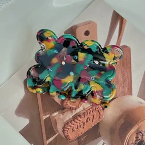 Detailed close-up view of a colorful marbled acetate hair claw with sparkling rhinestones.
