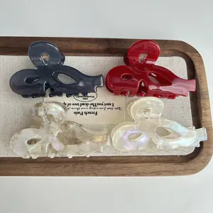 Close-up of asymmetric hollow bow hair claws in acetate, elegant details on a wooden tray.