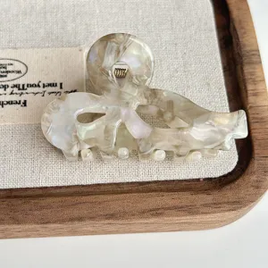Acetate hair claw clip with elegant hollow bow design and pearlescent marble texture.