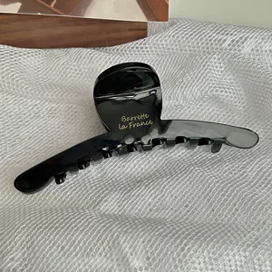 Large black acetate hair claw clip with golden letter print, elegant French style accessory.