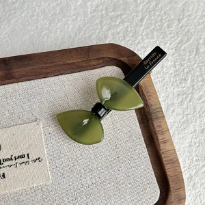 Close-up detail view of the green resin bow hair clip resting on a fabric-lined wooden tray.