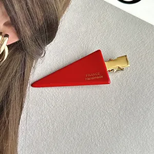 Red triangle hair clip with gold metal duckbill clip, elegant side hair styling detail shot.