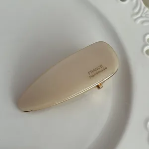 Close-up view of a minimalist beige acetate hair clip, surface lisse and gold print.