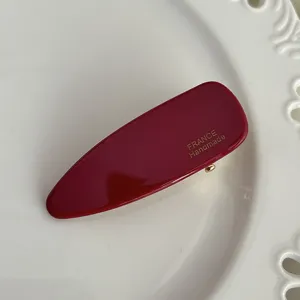 Close-up detail of the elegant dark red acetate hair clip with gold stamped typography.