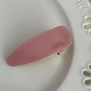 Detailed view of the pink acetate triangle hair clip, featuring a gold border and handmade text.