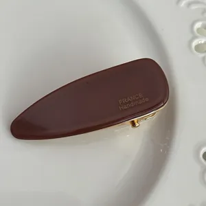 Detail view of a French retro brown acetate triangular hair clip with gold accent for women.