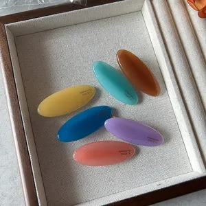 Set di sei mollette per capelli ovali minimaliste e colorate, esposte in vassoio.