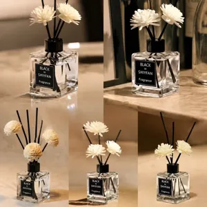 Botella difusora de vidrio transparente con tapa negra y varillas de flores blancas para el hogar.