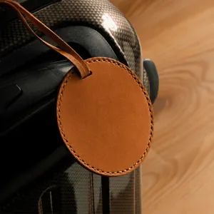 Gros plan détaillé d'une étiquette de bagage ronde en cuir PU marron sur une poignée de valise.
