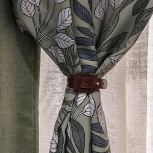 Close-up of brown PU leather curtain tieback buckle strap holding decorative leaf print drapery panel