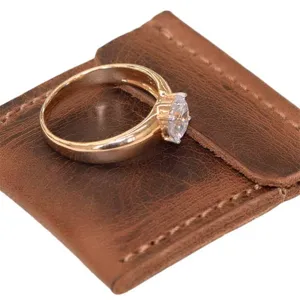 Details of a rose gold ring with a clear stone displayed on a vintage brown leather pouch.