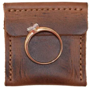 Close-up detail of a delicate ring resting on a vintage brown leather pouch, elegant style.